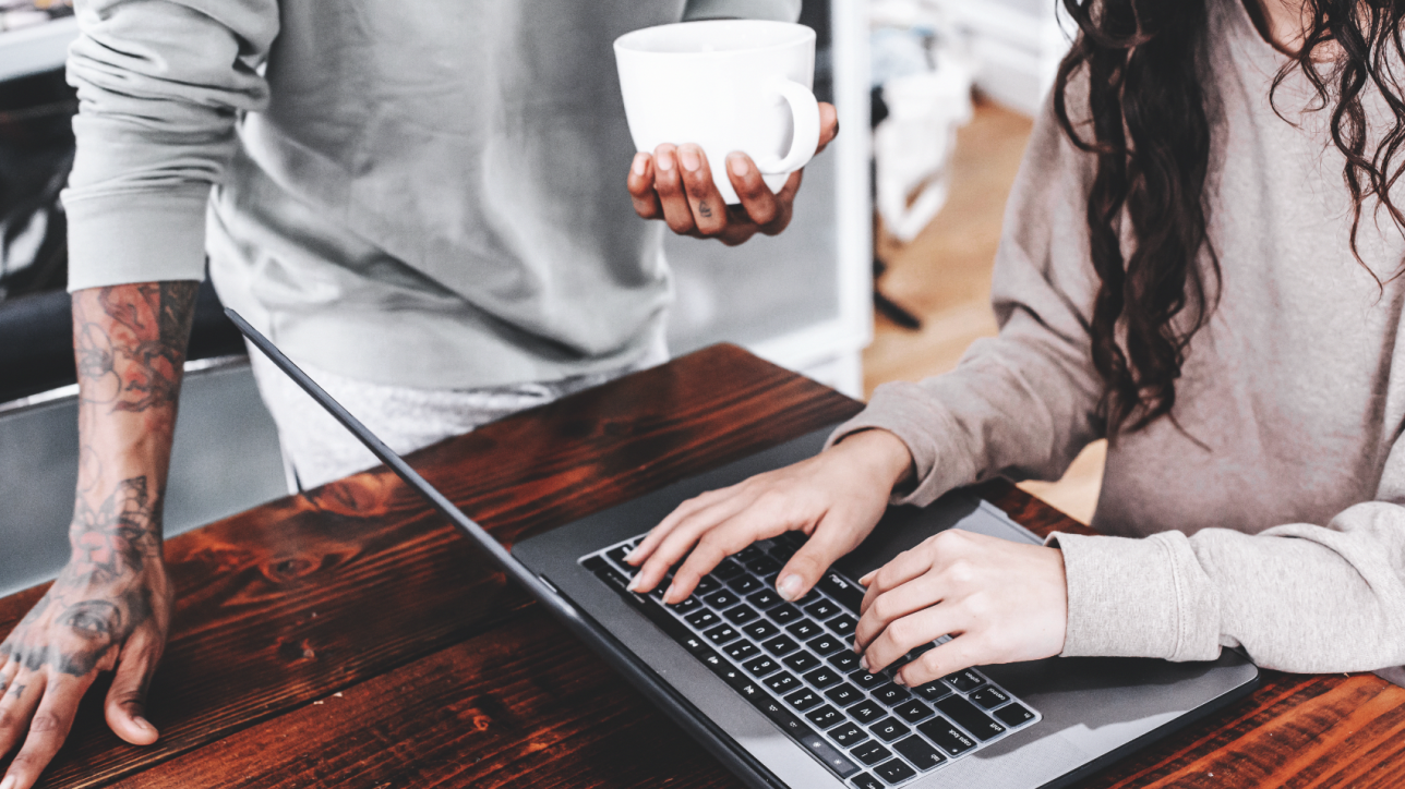 woman's hand typing on laptop, man standing next to her